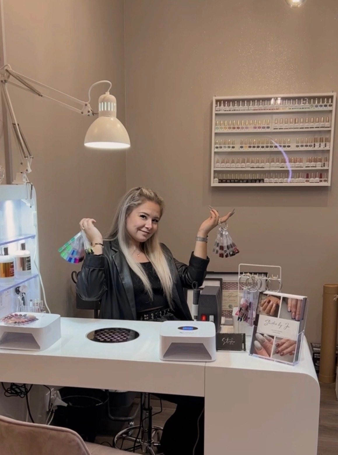 Justine à son poste de manucure, des nuanciers de couleurs dans chaque main